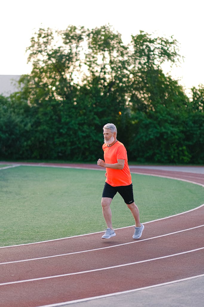 Full body of elderly male jogging in stadium surrounded with lush green bushes